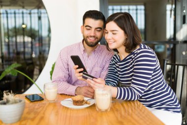 Heyecanlı çift akıllı telefondan online alışveriş yapıyor ve kafede kredi kartıyla ödeme yapıyor. 