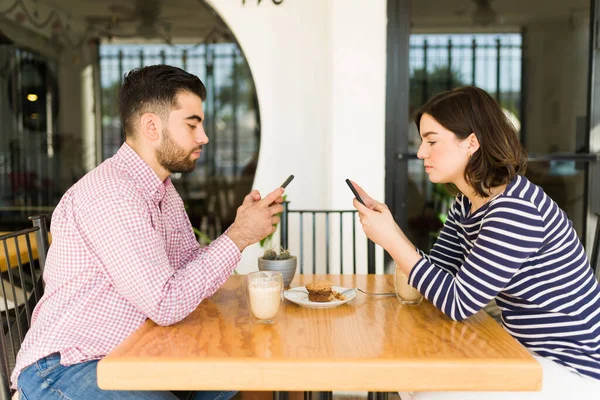 怒っている若い女性と男感じて退屈しながら日付コーヒーショップでと彼らのスマートフォン上のテキストメッセージ — ストック写真