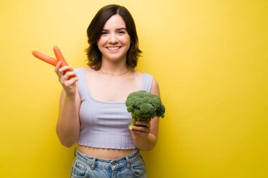 Sebze yiyen sağlıklı genç bir kadın. Havuç ve brokoli tutan güzel bir kadın.