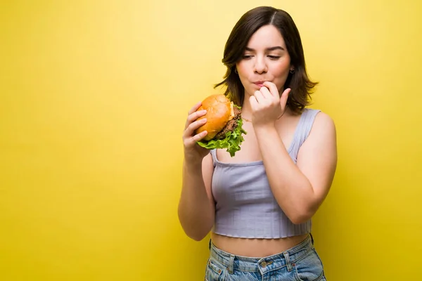 一个年轻貌美的女人 贪得无厌 一边舔着手指 一边吃着美味的汉堡包 — 图库照片