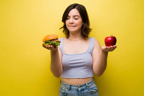 欲求やハンバーガーや健康的なリンゴを食べることを選択した美しい若い女性 — ストック写真