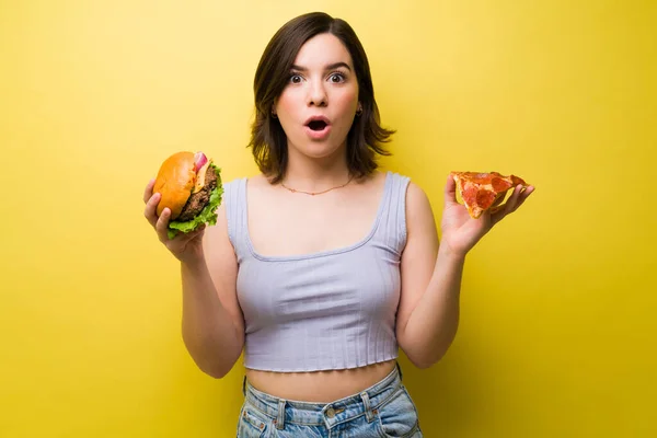 ハンバーガーやピザを食べることを選択した驚きの女性 おいしい食べ物を食べる女性の肖像画 — ストック写真