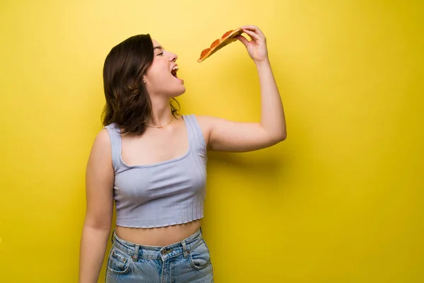 空腹若いです女性楽しみます食べることの大きなスライスのピザに対してAスタジオ黄色の背景 — ストック写真