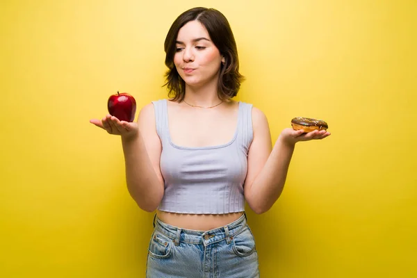 我应该吃什么 饥饿的女人一边拿着苹果和甜甜圈一边决定吃什么零食 — 图库照片
