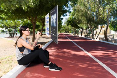 Virtual reality technology. Young woman resting from a workout and texting using augmented reality  clipart