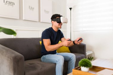 Yakışıklı Latin adam evde sanal gerçeklik oyunu oynamak için VR gözlük ve joystick kullanırken gülümsüyor.