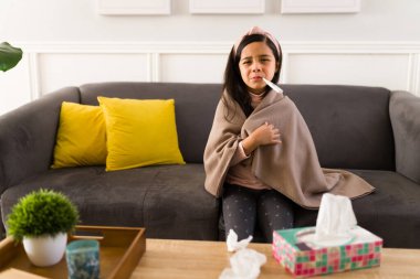 Yüksek ateş. İlkokul öğrencisi hasta, termometre kullanıyor ve evde ateşini ölçüyor.