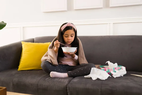 悪い寒さから回復しながらソファに座って熱いスープを食べる小学生の女の子 — ストック写真