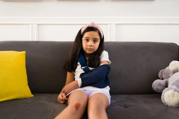 膝の傷を負った子供が片目で接触し腕のスリングを使って家で事故が起きた後 — ストック写真