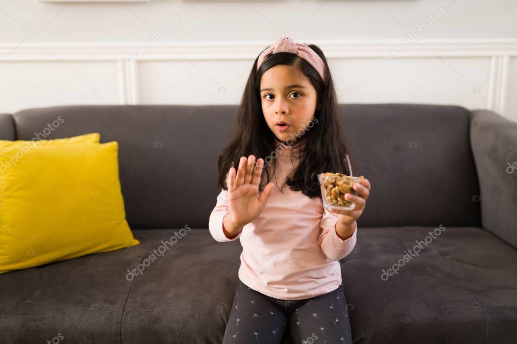Upset kid doesn't want to eat snacks. Sad girl refusing eating nuts and peanuts at home 