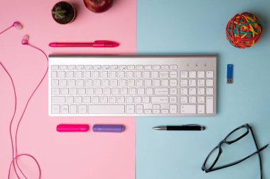 Onun ve onun ofis masası. Bilgisayar klavyesi, kulaklığı, gözlüğü ve kağıt kalemleri olan pembe ve mavi çalışma alanı.  