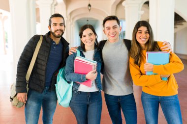 Attractive college friends smiling and hugging while carrying notebooks on their way to class