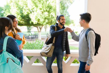 Hello! Cheerful college students giving a fist bump and saying hi after arriving for class in the morning