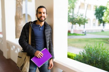 Handsome hispanic student carrying books and waiting for his college lecture on campus