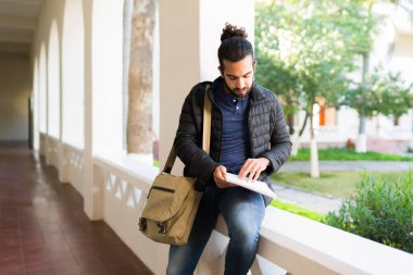 Busy male student checking his notes and homework while studying for a college exam in the campus