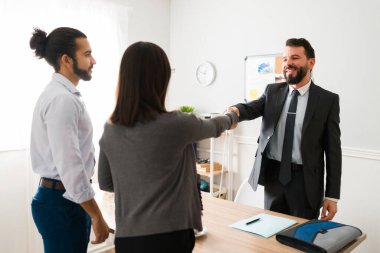 We got a deal. Latin couple shaking hands with a financial advisor and sealing a business contract 