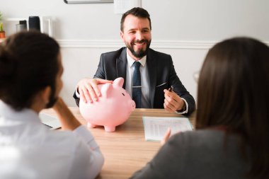 Happy finance advisor holding a piggy bank and investing money with a couple of clients
