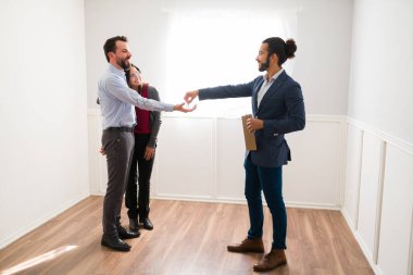 Burada çok mutlu olacağız. Yeni evli bir çiftin yeni evlerinin anahtarlarını bir satış temsilcisinden almasının yan görüntüsü.