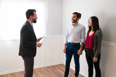 Emlakçı mutlu bir İspanyol kadın ve erkeğe ev gösteriyor. İlgilenen çift yeni bir ev almak istiyor.