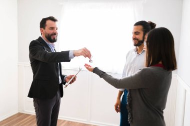 Yeni evinin tadını çıkar. Gülümseyen erkek emlakçı ve satış temsilcisi evin anahtarlarını birkaç alıcıya veriyor. 