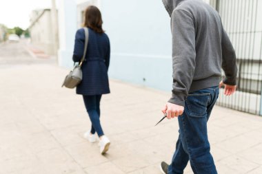Sokakta yalnız yürüyen genç bir kadını tehdit etmek ve çalmak için bıçak kullanan bir suçlunun arka görüntüsü.