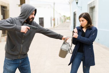 Şiddet ve güvensizlik. Silahlı saldırgan bir adam sokakta genç bir kadını gasp ediyor. Hırsız bir kurbanın çantasını çalıyor.