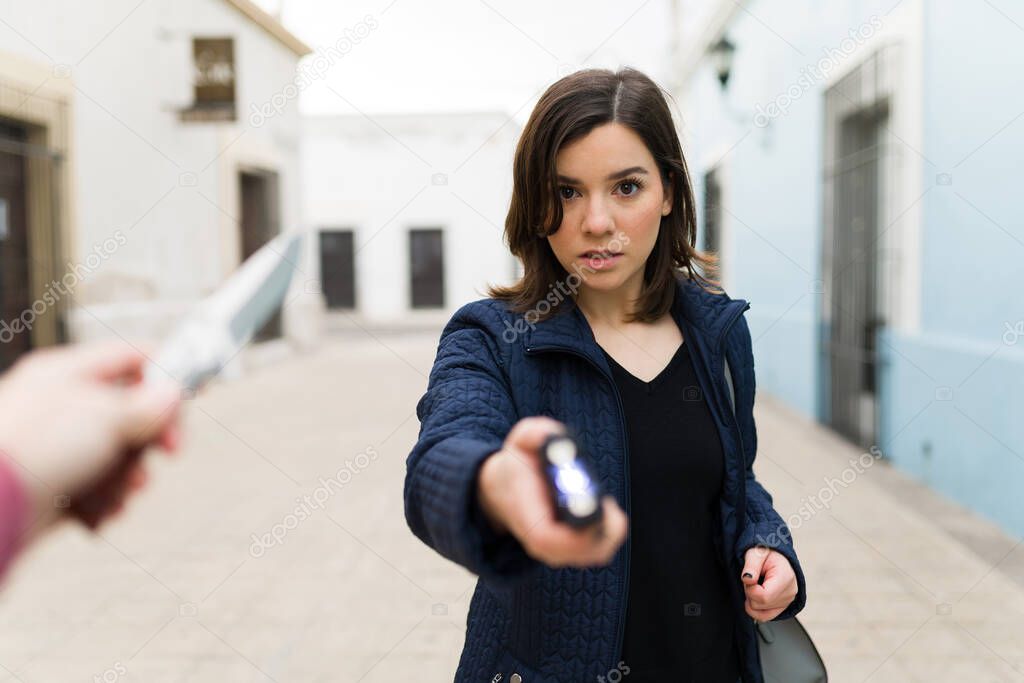 Afraid caucasian woman making eye contact and using a taser to defend herself from a criminal thief with a knife in the street
