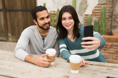 Kafkasyalı güzel bir kadın kafede kahve içerken Latin yakışıklı erkek arkadaşıyla selfie çekiyor.