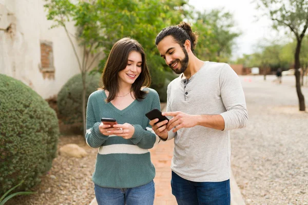 ラテン語のボーイフレンドと白人のガールフレンドは 彼らの携帯電話にテキストメッセージを笑顔 スマートフォンで写真を見せるハンサムな男 — ストック写真