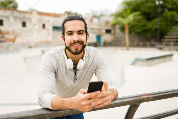 Jovem Bonito Usando Mídias Sociais Smartphone Sorrindo Enquanto Relaxa Livre — Fotografia de Stock