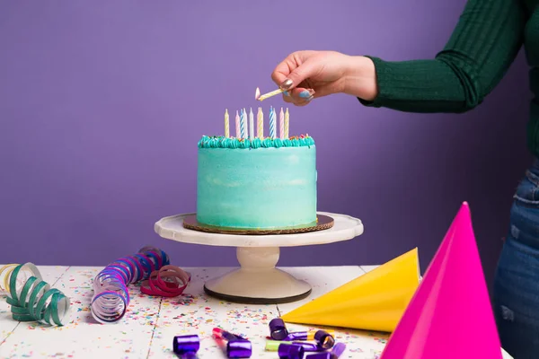 パーティーの帽子とサーペンタインで誕生日を祝うためにケーキの上にろうそくを灯す若い女性 — ストック写真
