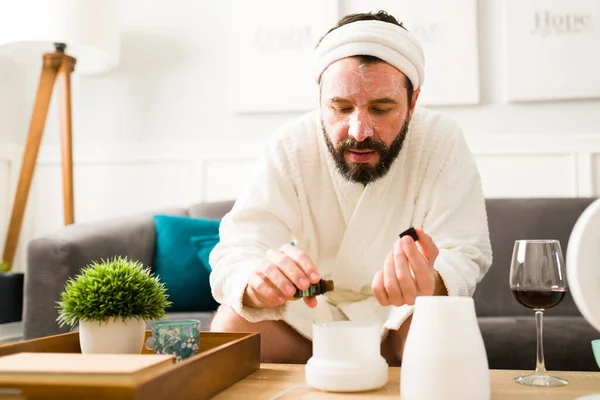 Handsome man with a white robe moisturizing his skin and putting essential oil in the aromatherapy diffuser