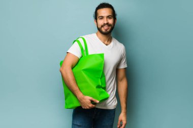 Alışverişe gitmek ve çevreye yardım etmek için yeşil bir alışveriş çantası kullanan neşeli genç adam.