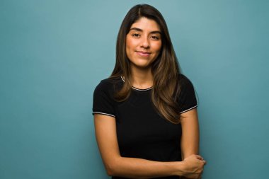 Stüdyoda genç ve güzel bir kadının göz teması kurup mavi bir arka plana gülümserkenki görüntüsü.