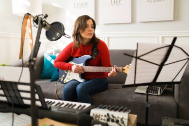 Yeni bir şarkı bestelerken elektro gitar çalan güzel bir bayan müzisyen. Müzik kağıdı kullanan genç bir kadın. 