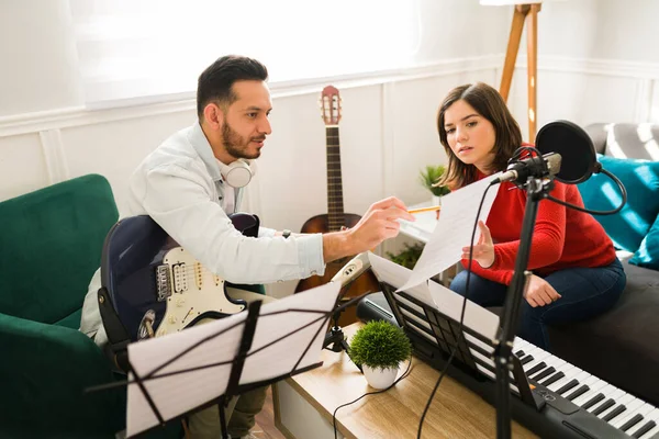 Writing the lyrics of a song. Attractive woman and man composing a new song on a music sheet while playing instruments