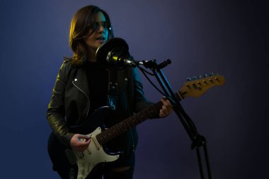 Çekici rock and roll kadın şarkıcısı elektro gitar çalarken bir şarkı kaydediyor. 
