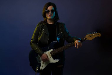 Siyah güneş gözlüklü çekici kadın elektro gitar çalarken göz teması kuruyor. 