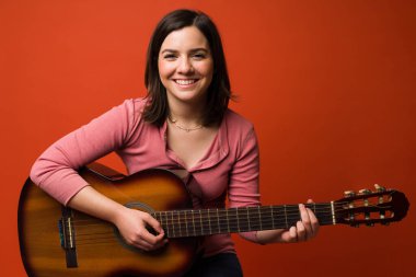 Neşeli yetenekli gitarist kameraya bakarken gülümsüyor ve akustik gitarıyla poz veriyor. 