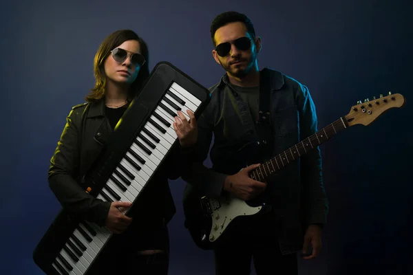 Artistic rock star showing her keyboard and young man playing the electric guitar before a rock concert