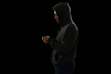 Siyah kapüşonlu şüpheli bir suçlunun akıllı telefondan mesajlaşmasının yan görüntüsü. 