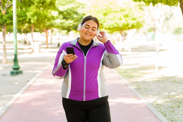 ワイヤレスヘッドフォンで音楽を聴きながら公園でリラックスした肥満の女性の笑顔とジョギング — ストック写真