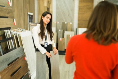 Muhteşem bayan satış temsilcisi mağazadaki yeni ahşap döşemeleri bazı müşterilere gösteriyor.