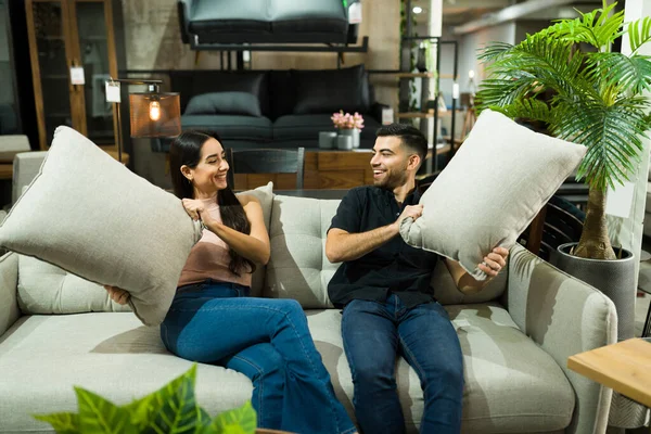 购物的时候玩得开心 快乐的女人和男人坐在家具店的沙发上玩着垫子 — 图库照片