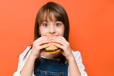 Hamburgeri ısıran küçük bir kızın yakınından ve gözleri açık şekilde tadını çıkarırken.