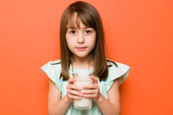 靠近一个可爱的小女孩 她在工作室里拿着一杯牛奶 眼神严肃地看着我 — 图库照片