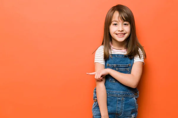 スタジオに立つ幸せな女の子の肖像画と横にコピースペースを指す — ストック写真