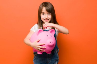 Finansal açıdan zeki küçük bir kız kumbarasına bozuk para atıyor ve birikimlerini arttırıyor.