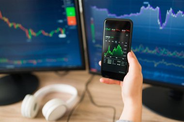 Yatırım yaparken ve borsanın yükselişini kontrol ederken akıllı telefonunu tutan Z jenerasyonundan bir kadın görülüyor. 