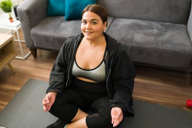 İspanyol kadın evde meditasyon yapmaya hazır. Hareketli giysili mutlu obez kadın yoga egzersizi için hazırlanıyor.